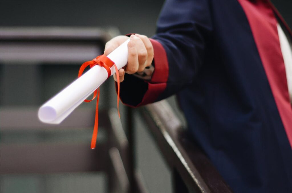 A close-up image of a graduate holding a diploma tied with a red ribbon, symbolizing achievement and success.